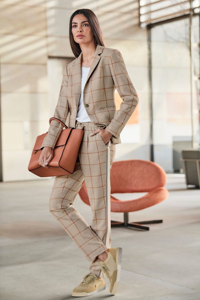 Frau im Büro-Outfit mit Hosenanzug im Glencheck-Muster, Tasche und Sneakern